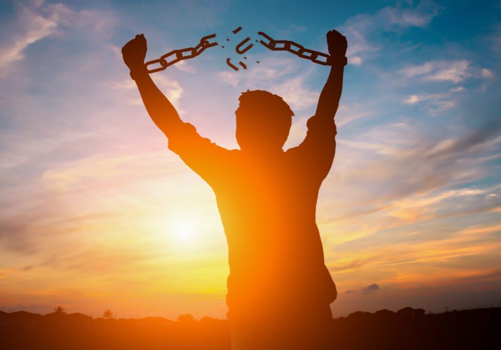 Silhouette image of a businessman with broken chains in sunset